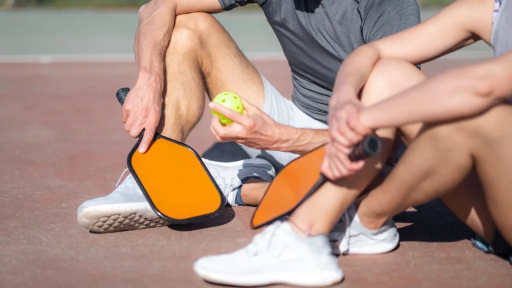 Arizona- two people playing pickleball sitting on court resting. New pet-friendly apartment homes for rent with private fenced backyards in Arizona with pool, pickleball, dog park, gym, clubhouse and gated community. *No breed or weight restrictions. Yardly